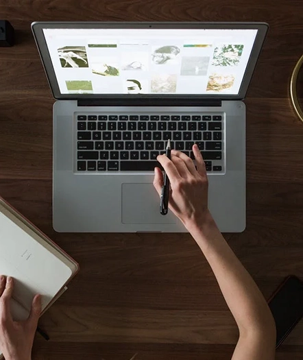 a hand typing on a laptop, whilst making notes in a book with their other hand